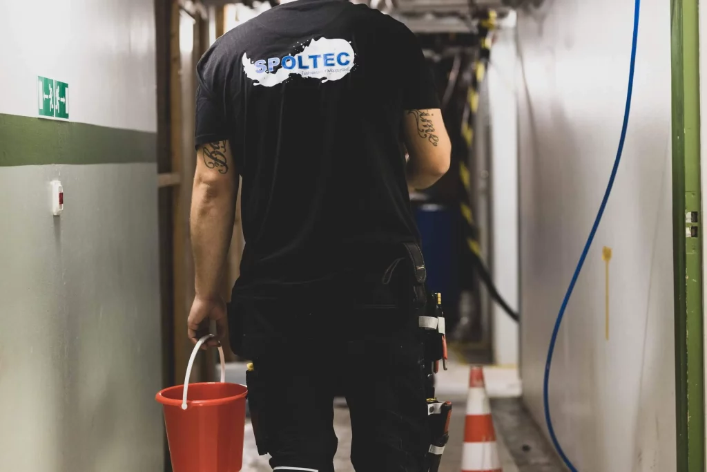 Person i en hall som bär en röd hink med byggverktyg på bältet.